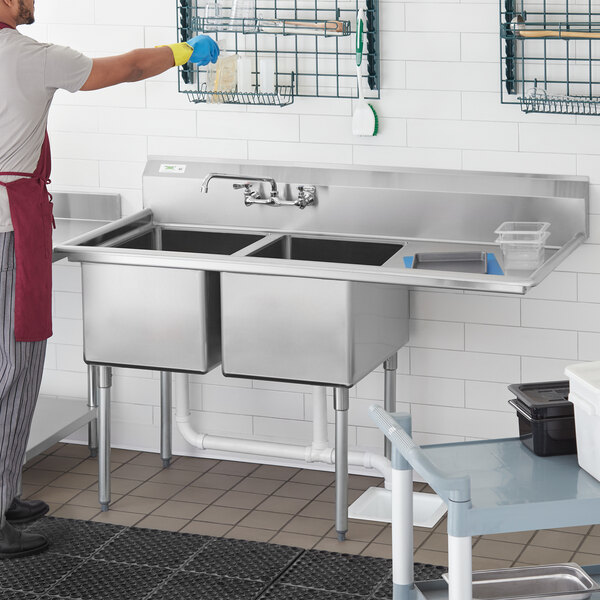 A man in a white apron washing a Regency stainless steel 2 compartment sink.