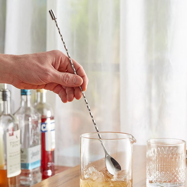 A hand using an Acopa silver weighted bar spoon to stir a cocktail in a glass of ice.