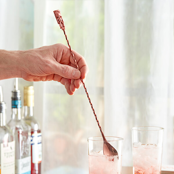 A hand using an Acopa copper weighted bar spoon with a tiki end to stir a cocktail.