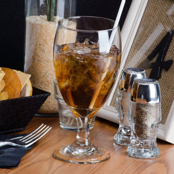 A Libbey Iced Tea Glass filled with brown liquid and ice on a table with salt and pepper shakers.