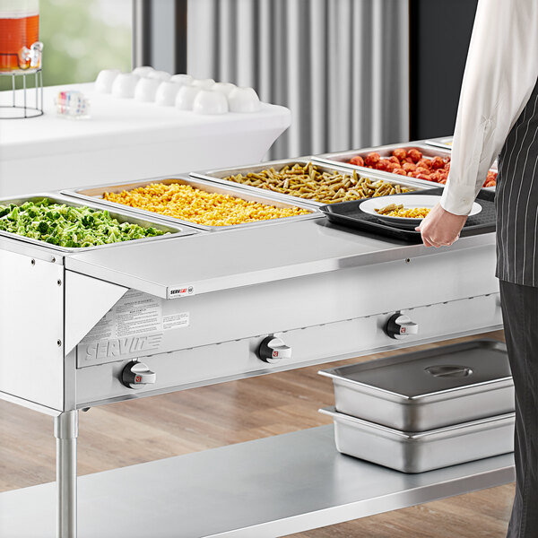 A man using a ServIt solid tray slide on a buffet table with metal containers.