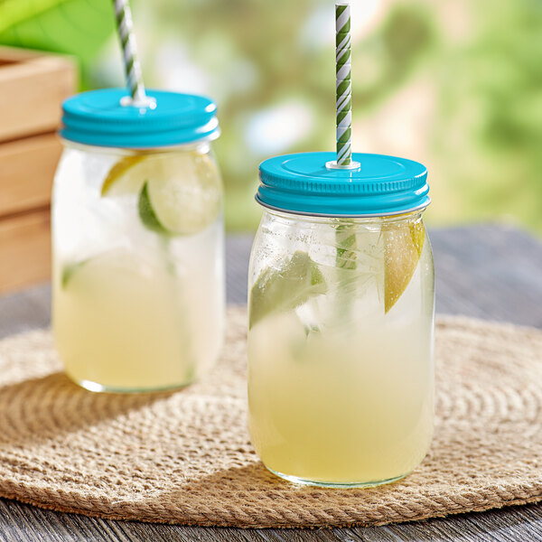 Two Acopa glass drinking jars with straws filled with limeade and lemons.