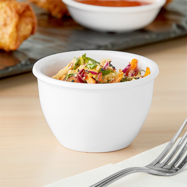 A white round melamine sauce cup filled with salad on a table with a fork.