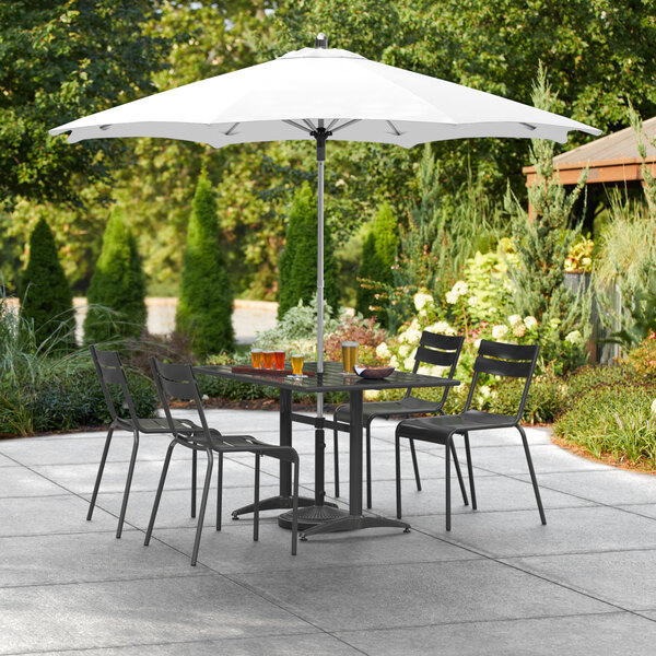 A white Lancaster Table & Seating umbrella over a table and chairs on an outdoor patio.