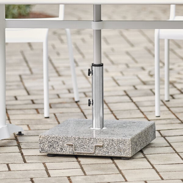 A white table with a Lancaster Table & Seating gray granite umbrella base on a brick patio.