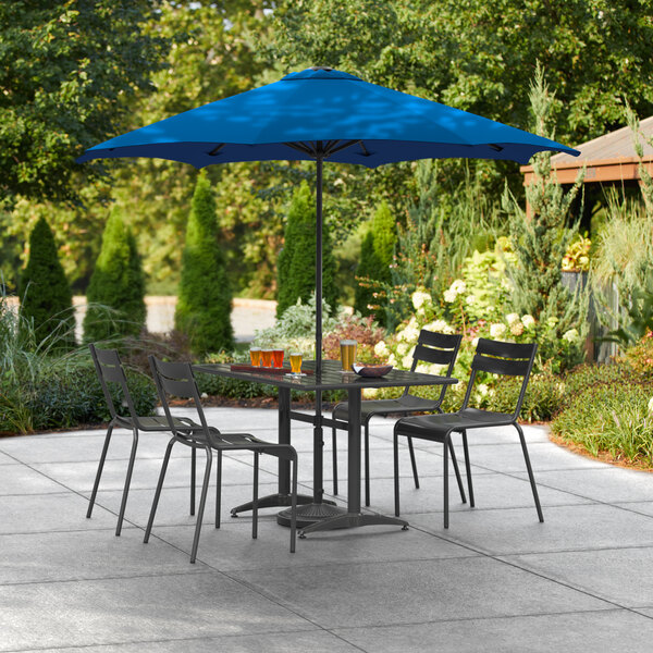 A Lancaster Table & Seating Pacific Blue umbrella over a table and chairs on an outdoor patio.