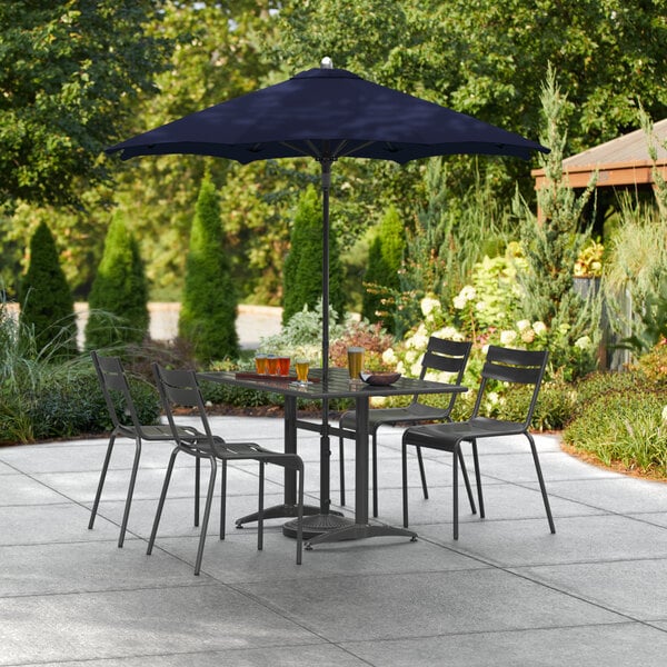 A Lancaster Table & Seating navy blue umbrella on a patio table with chairs.
