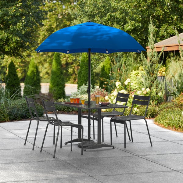 A blue Lancaster Table & Seating umbrella over a table and chairs on an outdoor patio.