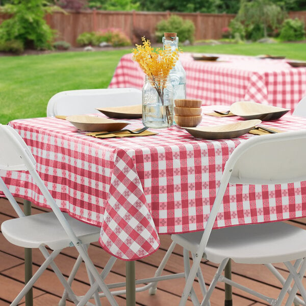 A table set with a burgundy checkered vinyl tablecloth on a table outdoors.
