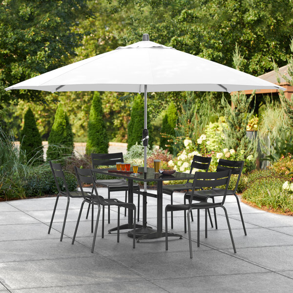 A table and chairs under a Lancaster Table & Seating white umbrella on a patio.