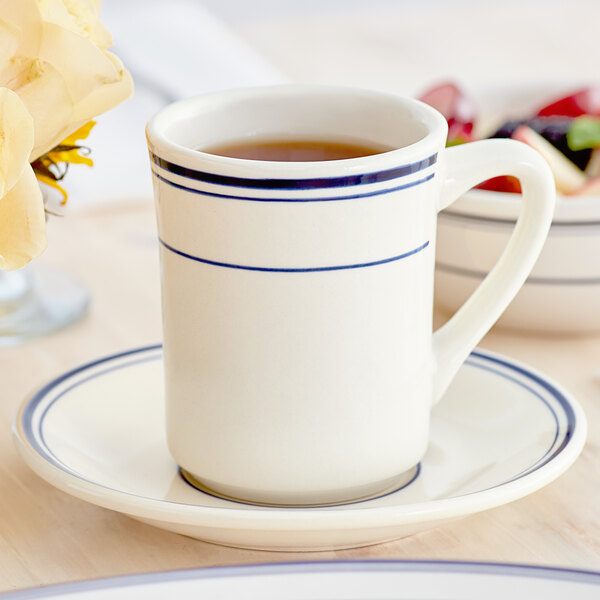 An Acopa ivory stoneware cup with blue bands on a saucer.