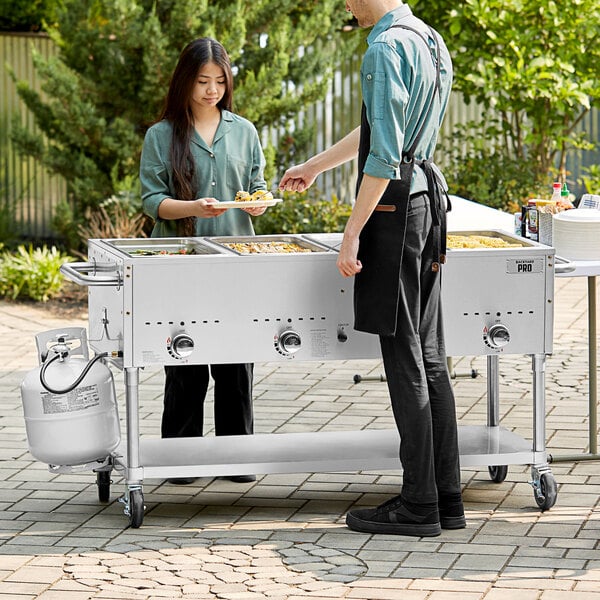 A man and woman using a Backyard Pro outdoor steam table at a catering event.