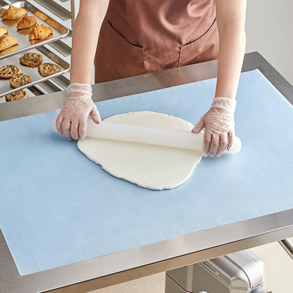 A woman rolling out dough on a blue Baker's Lane silicone work mat.