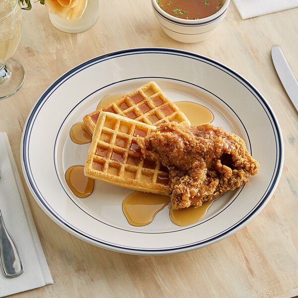 An Acopa ivory stoneware plate with blue bands holding fried chicken and waffles.