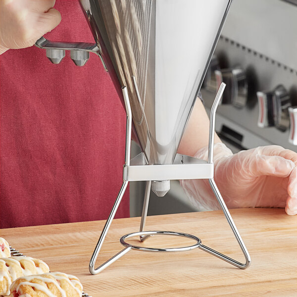 A person holding a Choice stainless steel confectionery dispenser funnel stand over a table with doughnuts.
