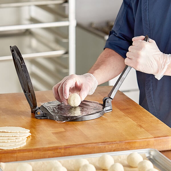 A person using a Choice cast iron tortilla press to press dough on a counter.
