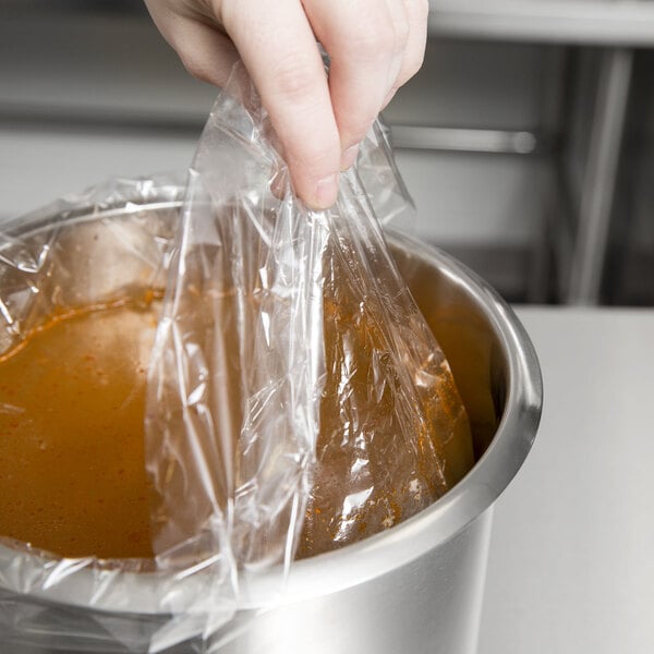 A hand holding a plastic bag over a pot of soup.