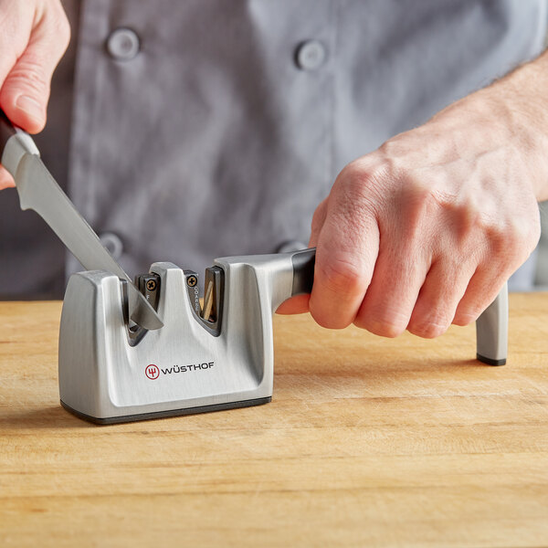 A person's hand using a Wusthof knife sharpener to sharpen a knife.