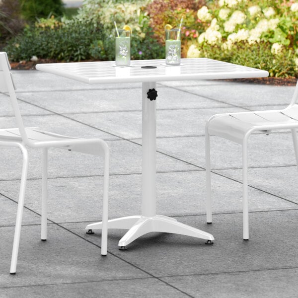 A white table with a black umbrella hole on a patio with two white chairs.