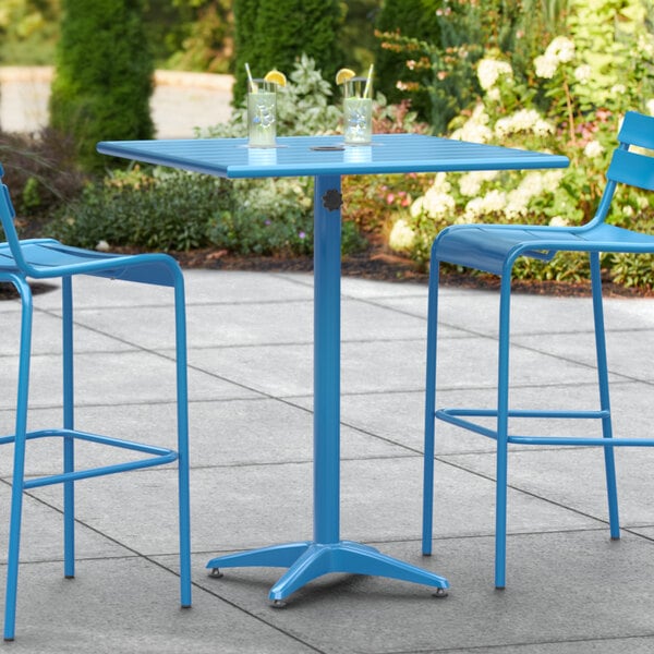 A blue Lancaster Table & Seating bar height table with two chairs on a patio.