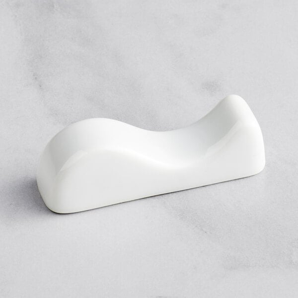 A Bauscher bright white porcelain chopstick rest with a curved edge on a white surface.