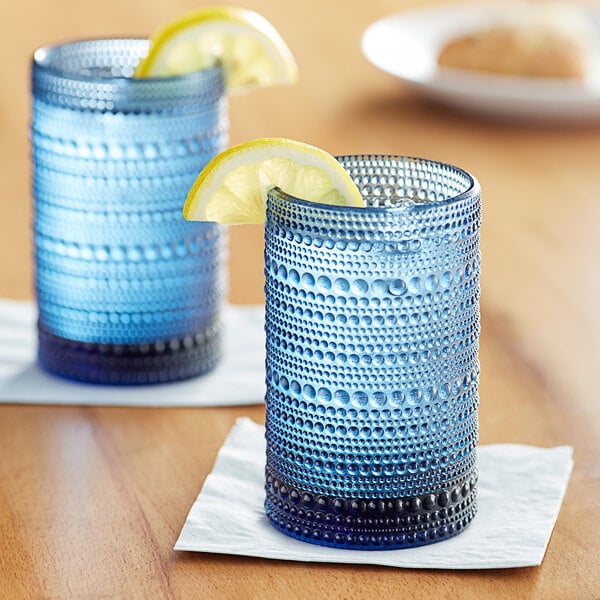 Two Fortessa cornflower blue beverage glasses on a table with lemon wedges.