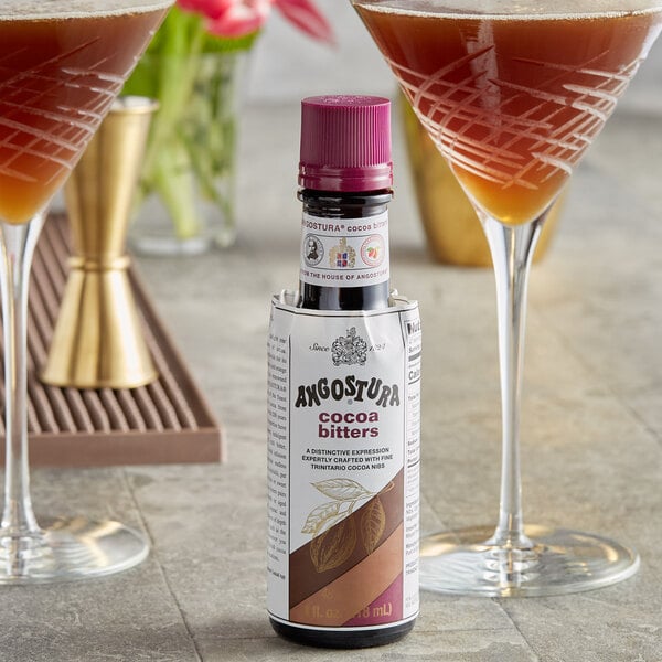 A bottle of Angostura Cocoa Bitters next to two glasses of liquid.