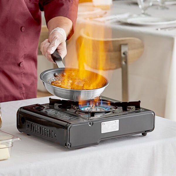 A person cooking food in a pan on a Choice portable gas stove.