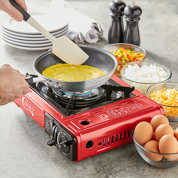 A hand using a spatula to cook an omelette in a pan on a Choice portable stove.