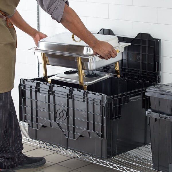 A person holding a metal container with food in a black Choice stackable storage box.
