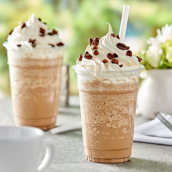 A white coffee cup filled with brown Capora Coffee Frappe mix topped with whipped cream.