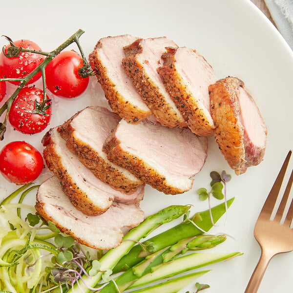 Sliced Maple Leaf Farms boneless duck breast on a plate with tomatoes and green beans.