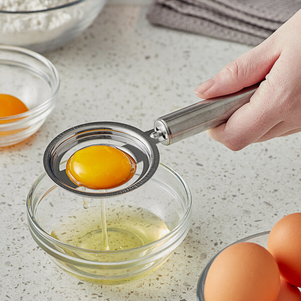 A person using a Choice stainless steel egg separator to separate a yolk over a bowl of eggs.