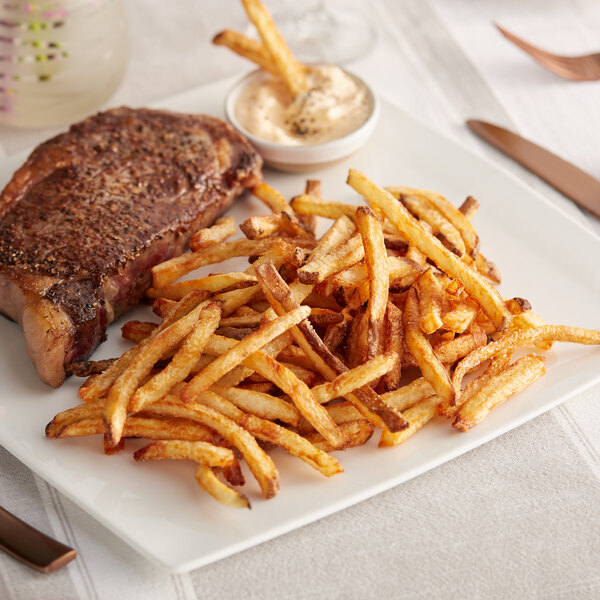 A plate of steak and french fries with a knife and fork.