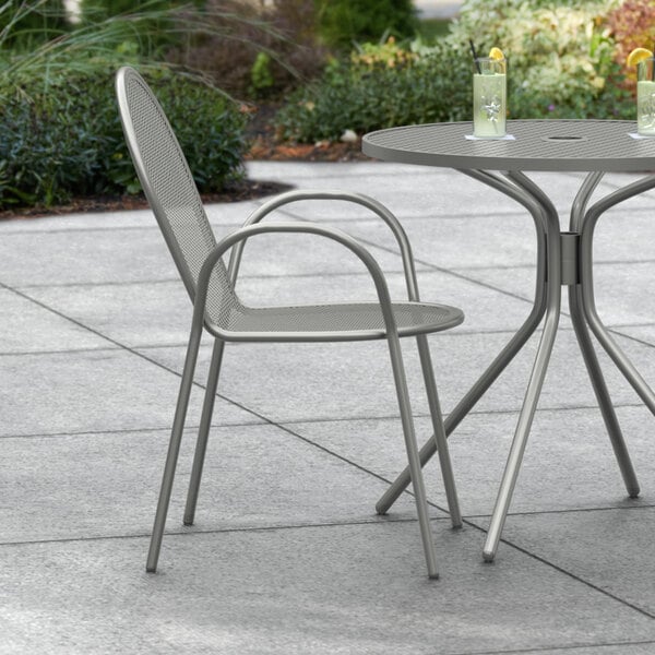 A Lancaster Table & Seating Harbor Gray outdoor arm chair and table on a patio.