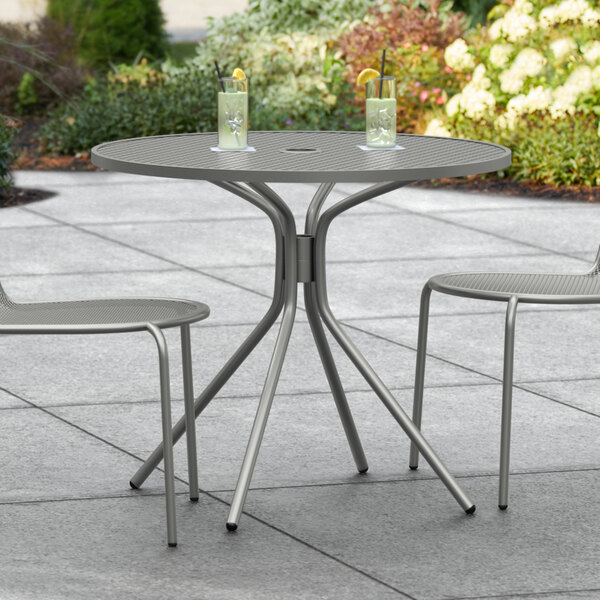A Lancaster Table & Seating Harbor Gray outdoor table with two chairs on a patio.