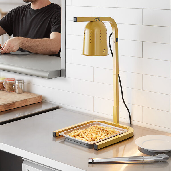 A man using an Avantco gold free standing heat lamp to cook food on a counter in a professional kitchen.