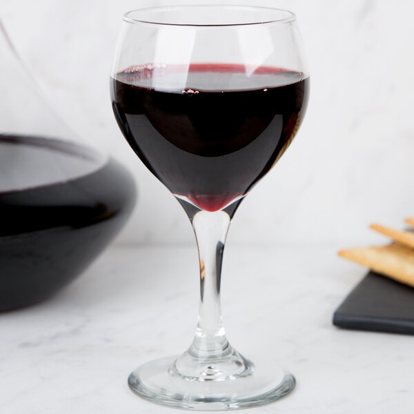 A Libbey red wine glass filled with red wine on a table in a winery cellar.
