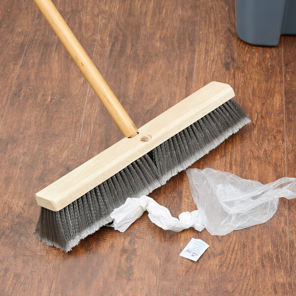 A Carlisle commercial broom head with gray flagged bristles on the floor.