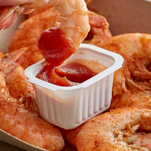 A shrimp in a container of cocktail sauce.