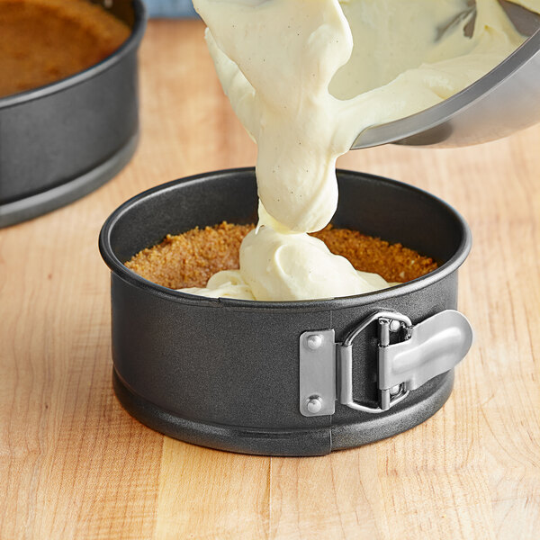 A person pouring white cream into a Choice springform cake pan.