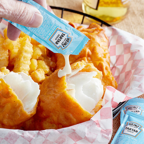 A hand holding a Heinz Tartar Sauce packet over fried food.