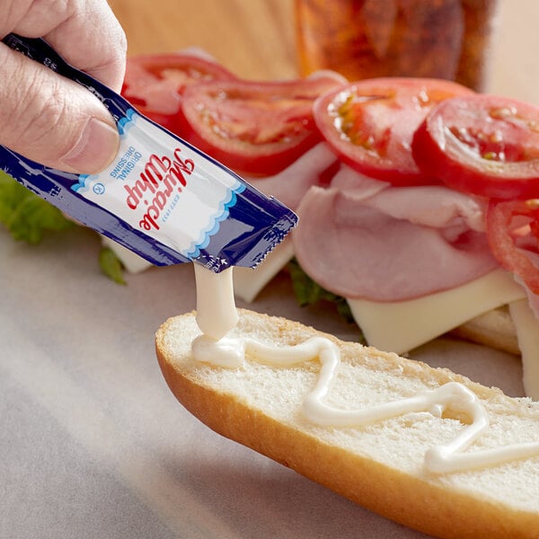 A person pouring Kraft Miracle Whip on a sandwich.