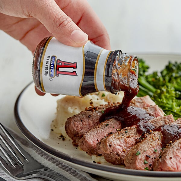 A hand pouring A.1. Original Steak Sauce onto a plate of meat.