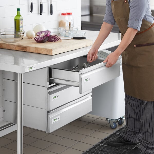 A woman in an apron opening a Regency stainless steel drawer in a kitchen counter.