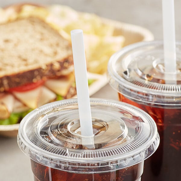 A plastic straw in a plastic cup with a sandwich.