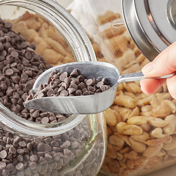 A person using a Choice aluminum scoop to scoop chocolate chips into a jar.