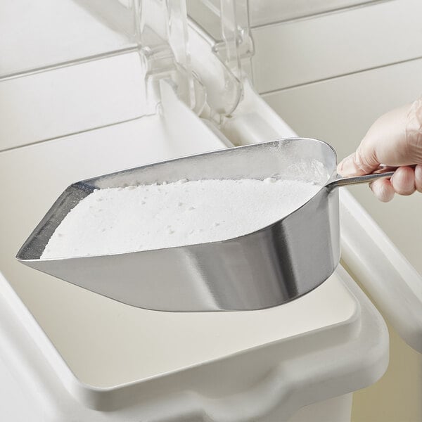 A person's hand holding a Choice flat bottom aluminum scoop filled with white powder.