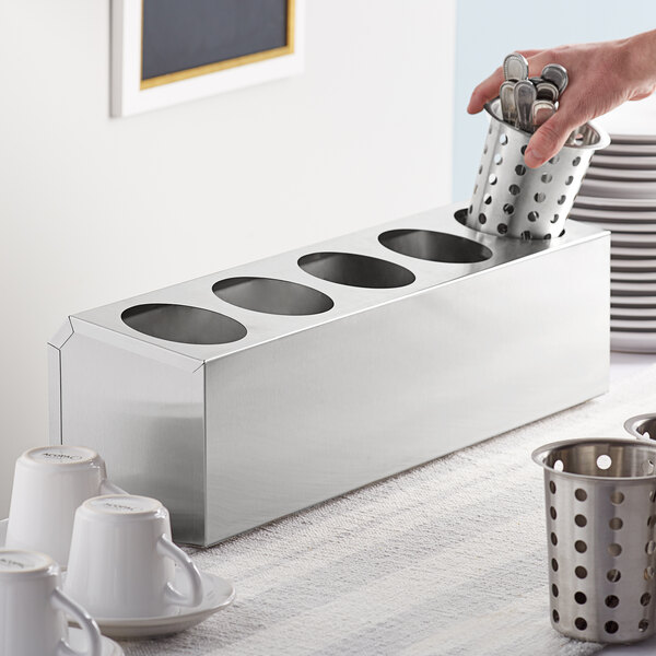 A hand putting spoons into a stainless steel flatware organizer with holes.