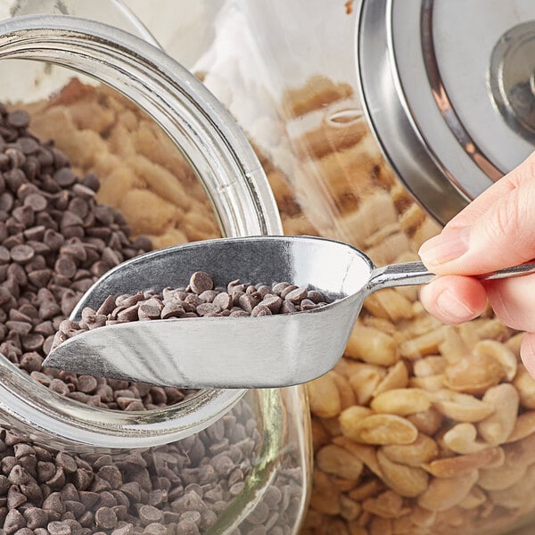 A person using a Choice aluminum flat bottom scoop to pick up chocolate chips.